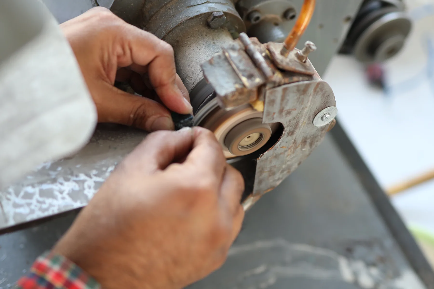 Macro view of a master cutter using a precise diamond saw to cut through a large rough emerald with sparks and water cooling